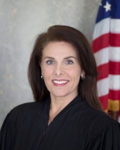 Image of a smiling woman wearing a judicial robe in front of an American flag