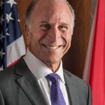 Smiling man wearing business attire, flag background