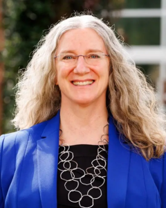 a woman with curly long hair wearing glasses and a blue jacket