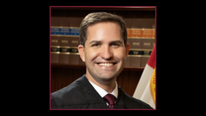 a man wearing a black judicial robe and tie smiling at the camera