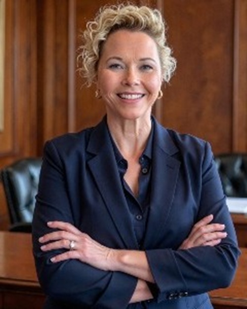 Stacey Salmons A woman with blond curly hair and arms crossed is standing in a courtroom