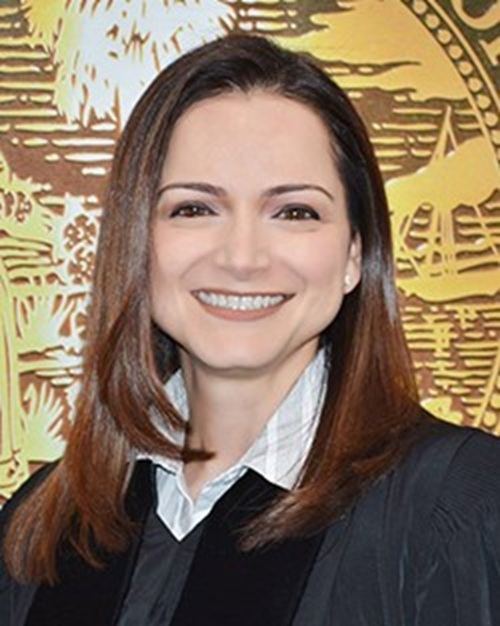 Lody Jean A woman with dark hair is wearing a judicial robe standing in front of a seal